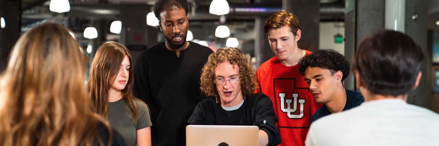 a group of students around a computer as one of them shows the others what they learned